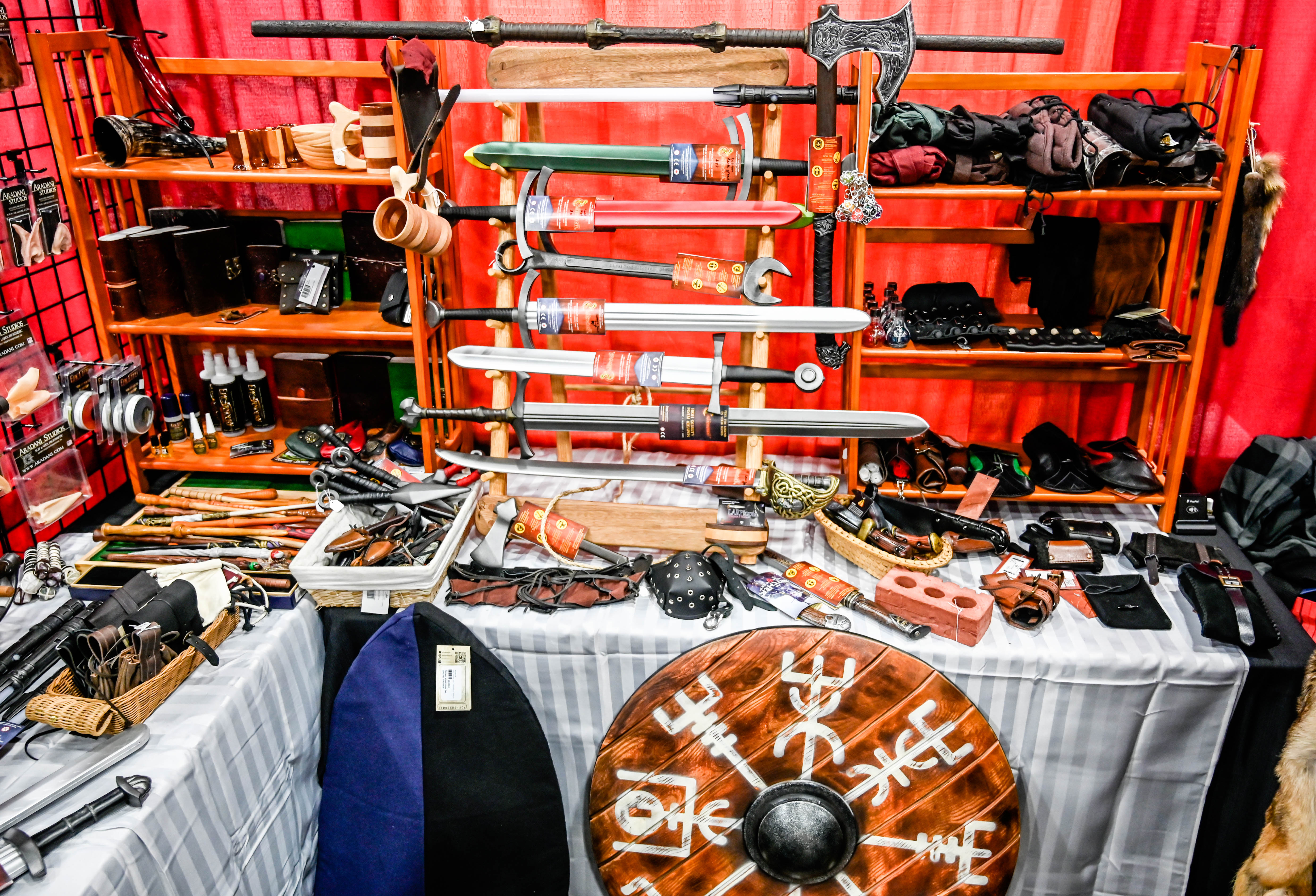youmacon 2019 larptopia booth with calimacil swords, daggers, axe, staff, brick, leather accessories, elf ears, potions, belt, gambeson, shield, pouch